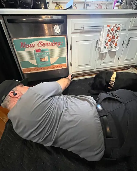 Our owner lying on a protective mat to work under a dishwasher, with a dog resting beside him