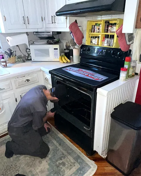 Technician kneeling at an electric range with a branded protective mat covering the cooktop